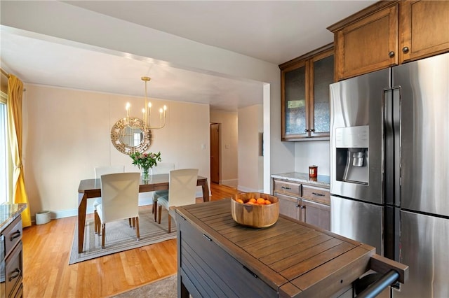 kitchen with light wood-type flooring, pendant lighting, stainless steel fridge with ice dispenser, glass insert cabinets, and a chandelier