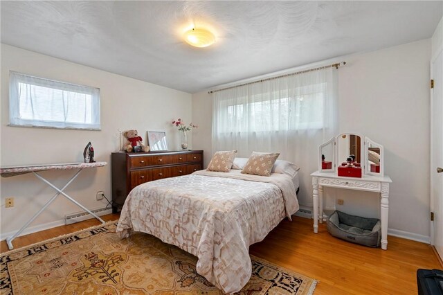 bedroom with a baseboard radiator, multiple windows, baseboards, and light wood-style flooring