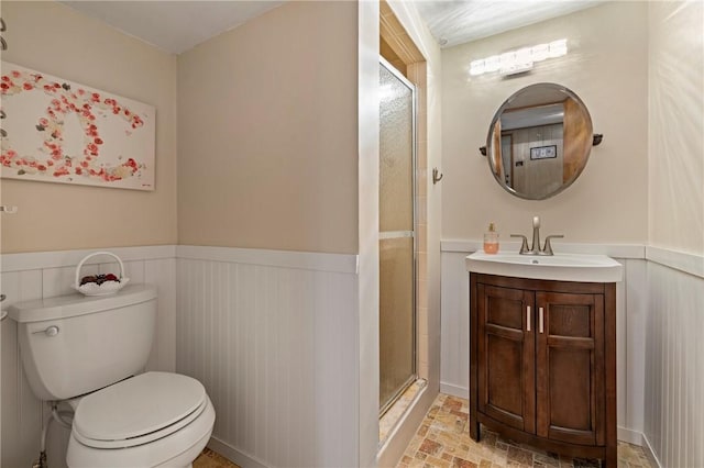 bathroom with vanity, toilet, a shower with shower door, and wainscoting