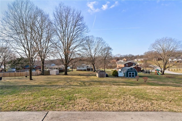 view of yard featuring a storage shed, an outbuilding, fence, and a residential view