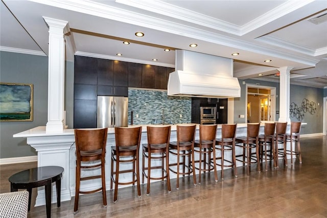 kitchen featuring custom exhaust hood, decorative columns, backsplash, and stainless steel appliances