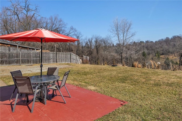 view of patio / terrace featuring a wooded view, outdoor dining area, and fence