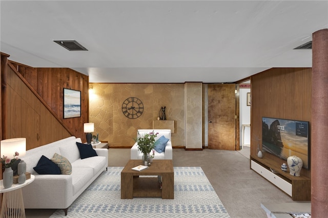 living room with stairs, light colored carpet, visible vents, and wood walls