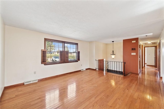 empty room featuring light wood-style floors, visible vents, and baseboards