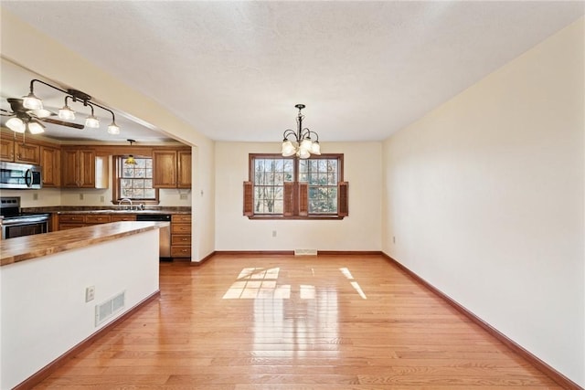 kitchen featuring visible vents, light wood-style flooring, appliances with stainless steel finishes, a notable chandelier, and brown cabinets