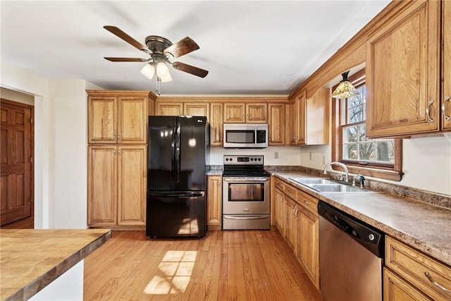 kitchen with brown cabinets, a sink, appliances with stainless steel finishes, light wood finished floors, and ceiling fan