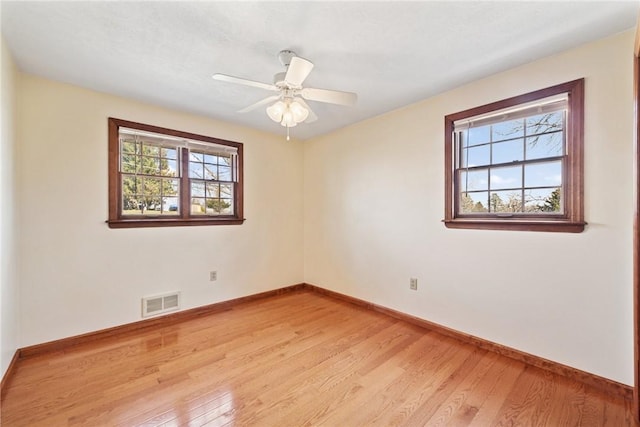 spare room with ceiling fan, visible vents, light wood-type flooring, and baseboards