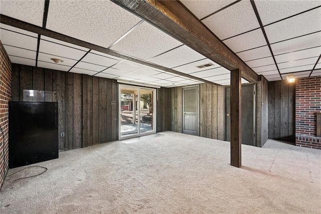 below grade area with a brick fireplace, a drop ceiling, wooden walls, and carpet floors