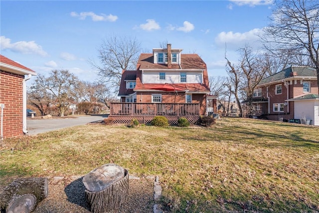 rear view of property with a lawn, a chimney, and a wooden deck