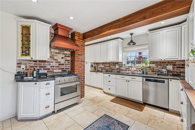 kitchen featuring white cabinets, premium range hood, appliances with stainless steel finishes, and a sink