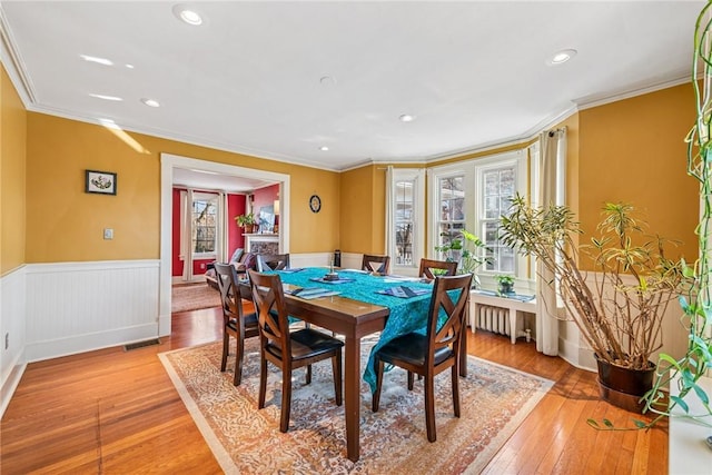 dining room featuring a wainscoted wall, visible vents, radiator heating unit, light wood-style floors, and crown molding