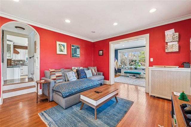 living area featuring arched walkways, crown molding, and hardwood / wood-style flooring