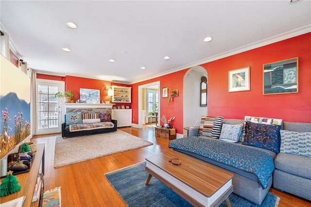 living room featuring recessed lighting, wood-type flooring, arched walkways, crown molding, and baseboards