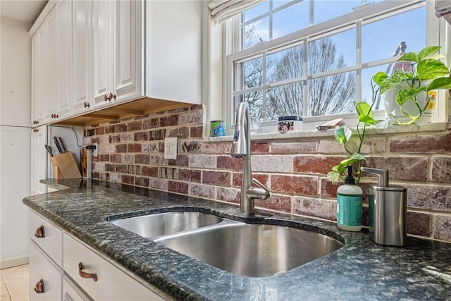 kitchen featuring dark stone countertops, a sink, tile patterned flooring, white cabinets, and backsplash