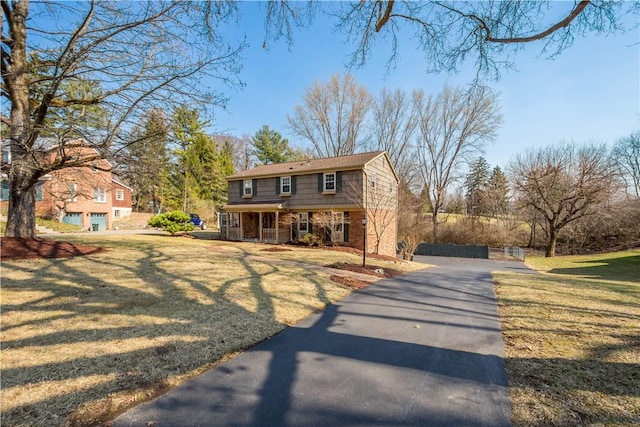 view of front of house featuring aphalt driveway, covered porch, brick siding, and a front yard