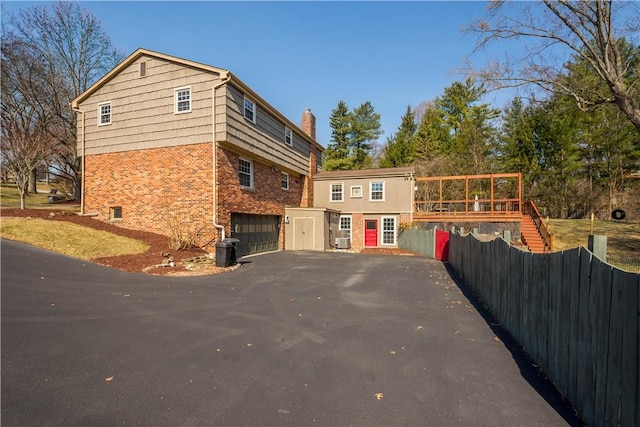 view of home's exterior with aphalt driveway, fence, a garage, brick siding, and a chimney