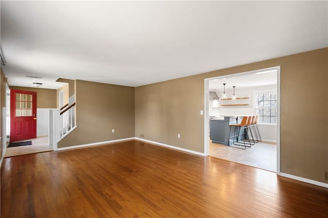 unfurnished living room featuring stairway, wood finished floors, and baseboards