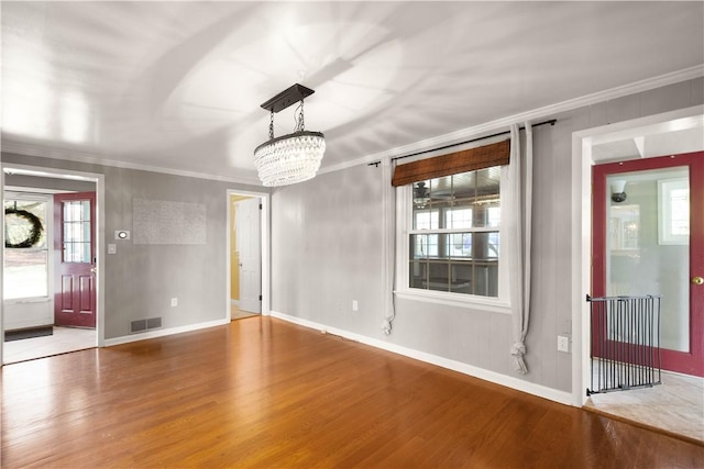 interior space with an inviting chandelier, wood finished floors, visible vents, and ornamental molding