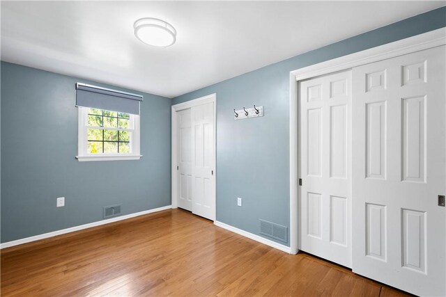 unfurnished bedroom featuring visible vents, baseboards, two closets, and wood finished floors