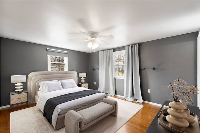 bedroom featuring multiple windows, ceiling fan, baseboards, and wood finished floors