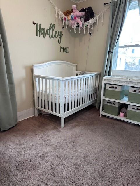 carpeted bedroom featuring a crib and baseboards