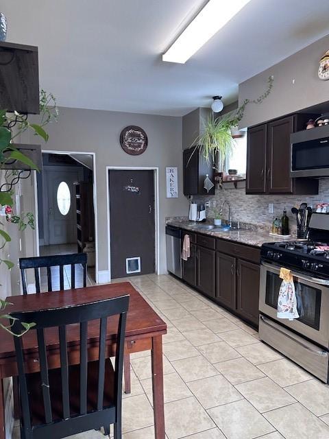 kitchen featuring light stone countertops, decorative backsplash, appliances with stainless steel finishes, light tile patterned flooring, and a sink