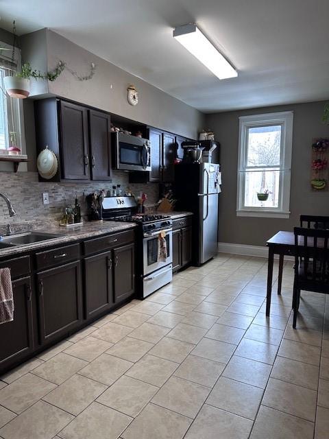 kitchen with dark countertops, light tile patterned floors, decorative backsplash, appliances with stainless steel finishes, and a sink