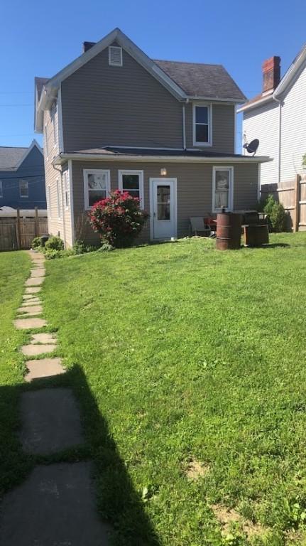 rear view of property with a lawn and fence