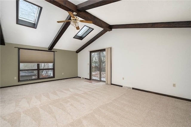 carpeted spare room featuring vaulted ceiling with skylight, baseboards, visible vents, and ceiling fan