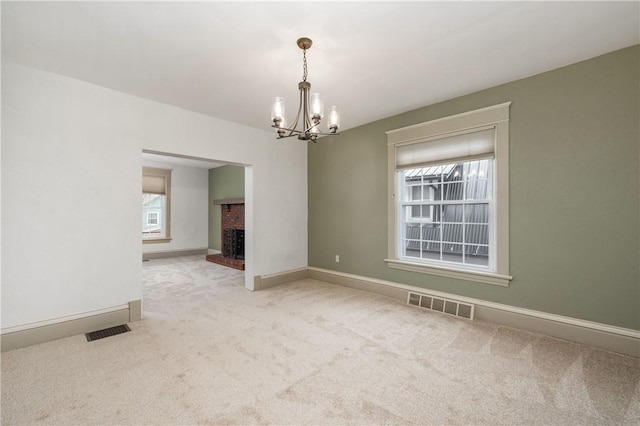 carpeted empty room featuring visible vents, baseboards, an inviting chandelier, and a fireplace