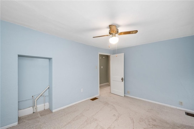 carpeted spare room with visible vents, baseboards, and ceiling fan