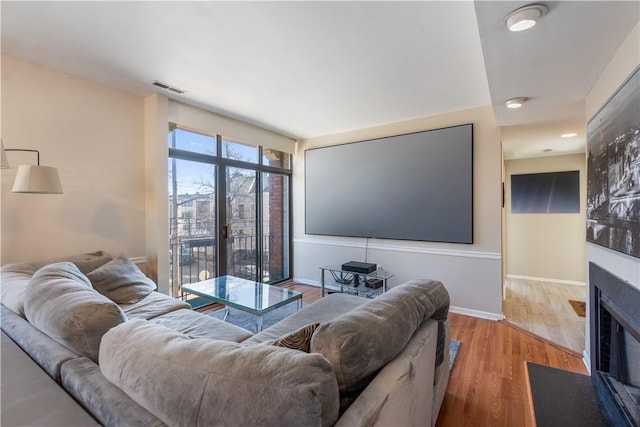 living area with visible vents, baseboards, wood finished floors, and a fireplace with flush hearth