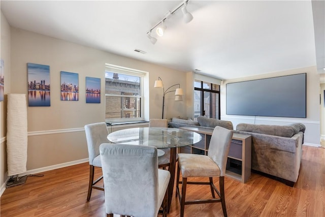 dining space featuring visible vents, rail lighting, wood finished floors, and baseboards