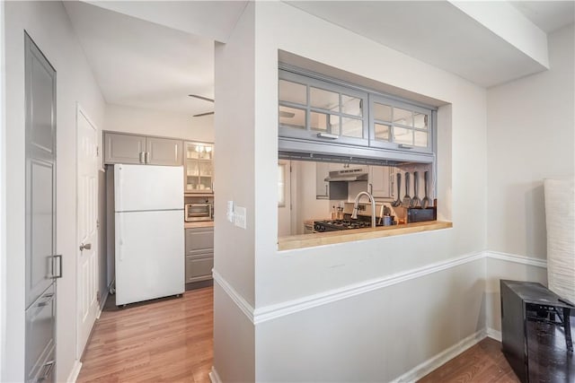 kitchen featuring under cabinet range hood, stainless steel appliances, light wood-style flooring, and gray cabinets