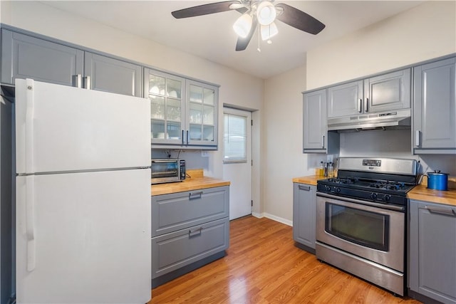 kitchen with under cabinet range hood, stainless steel gas range oven, freestanding refrigerator, and gray cabinetry