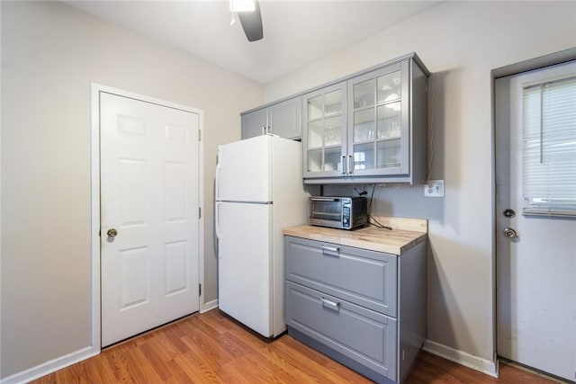 kitchen with a ceiling fan, a toaster, gray cabinets, freestanding refrigerator, and glass insert cabinets