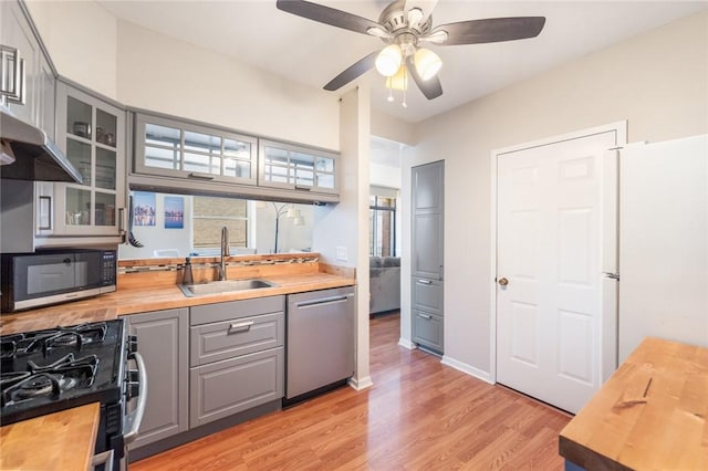 kitchen featuring wooden counters, gray cabinetry, a sink, black appliances, and glass insert cabinets