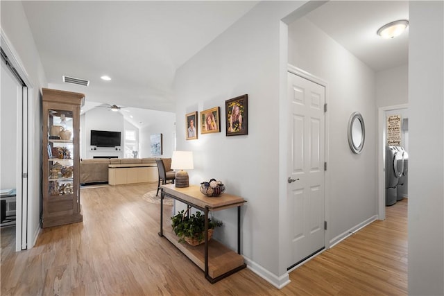 hall featuring visible vents, baseboards, vaulted ceiling, light wood-style flooring, and washer and dryer