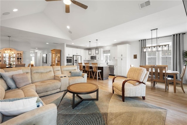 living room with visible vents, high vaulted ceiling, ceiling fan with notable chandelier, recessed lighting, and light wood finished floors