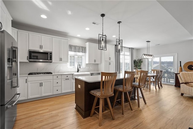 kitchen featuring light wood finished floors, a kitchen island, light countertops, appliances with stainless steel finishes, and white cabinetry