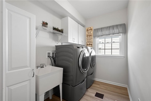 laundry area featuring baseboards, separate washer and dryer, light wood-style floors, cabinet space, and a sink