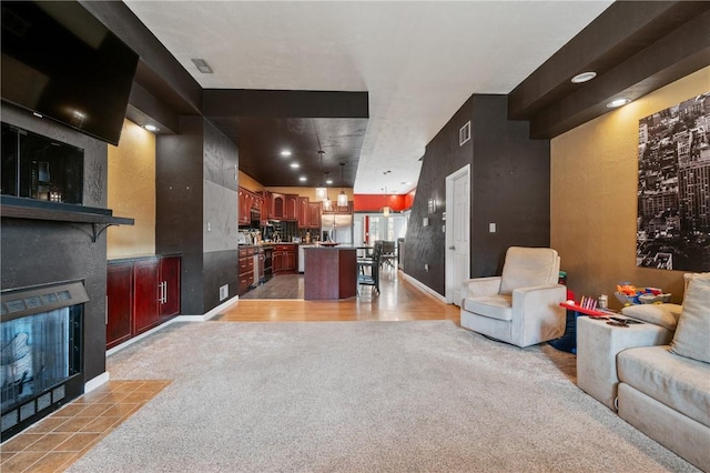 living room with a tiled fireplace, visible vents, light colored carpet, and baseboards