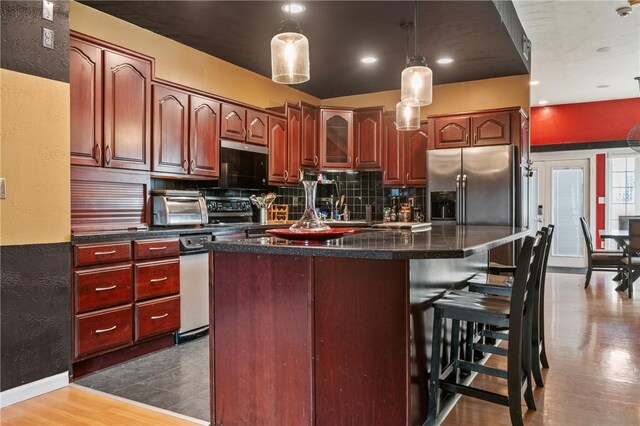 kitchen with dark countertops, tasteful backsplash, a center island, decorative light fixtures, and a kitchen breakfast bar