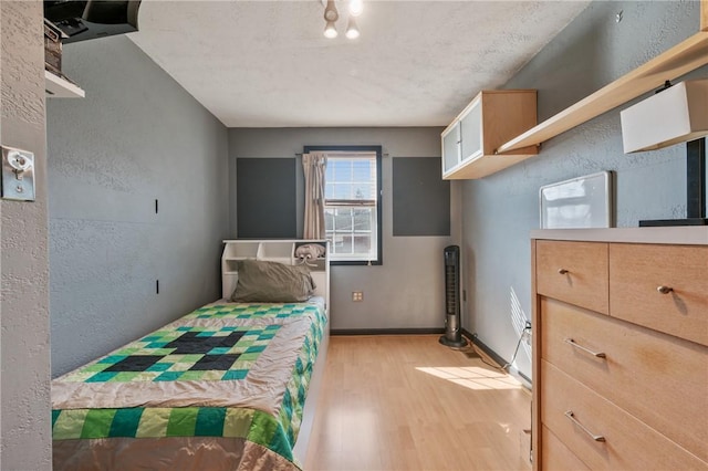 bedroom featuring light wood finished floors, baseboards, and a textured wall