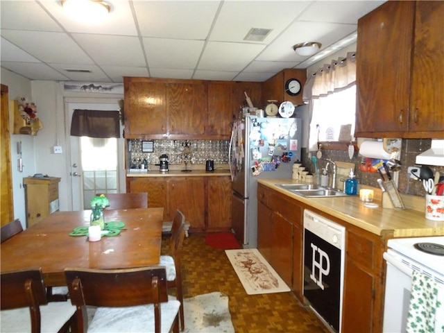 kitchen with dishwashing machine, freestanding refrigerator, a sink, under cabinet range hood, and brown cabinets