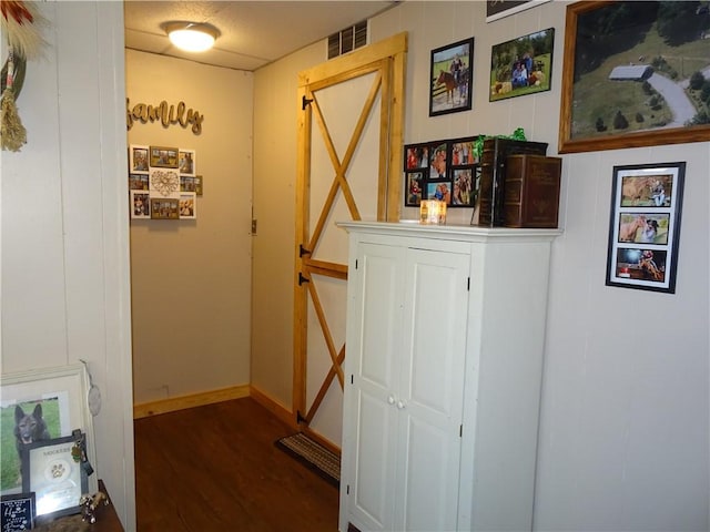 hallway with wood finished floors, visible vents, and baseboards