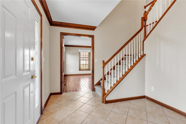 foyer entrance featuring light tile patterned flooring, crown molding, stairs, and baseboards