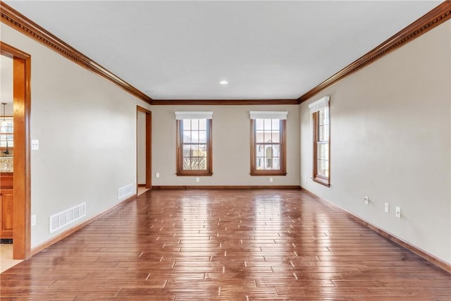 empty room with visible vents, crown molding, light wood-type flooring, and baseboards