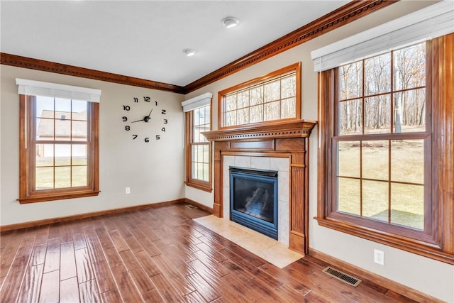 unfurnished living room with wood finished floors, visible vents, baseboards, a fireplace, and crown molding