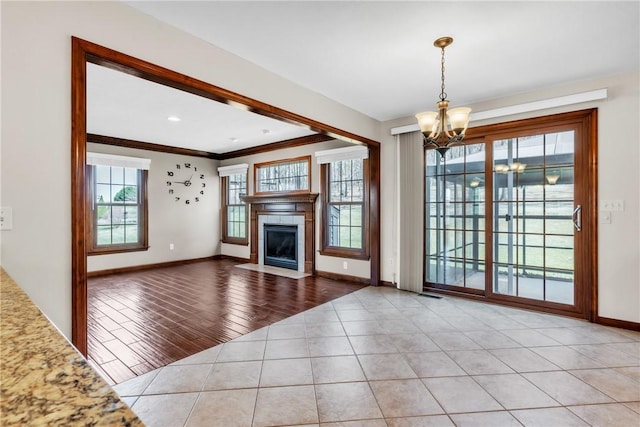 unfurnished living room featuring a fireplace with flush hearth, an inviting chandelier, crown molding, tile patterned flooring, and baseboards